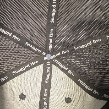 Close-up of a cap with 'Snagged Bro' branding on a black background
