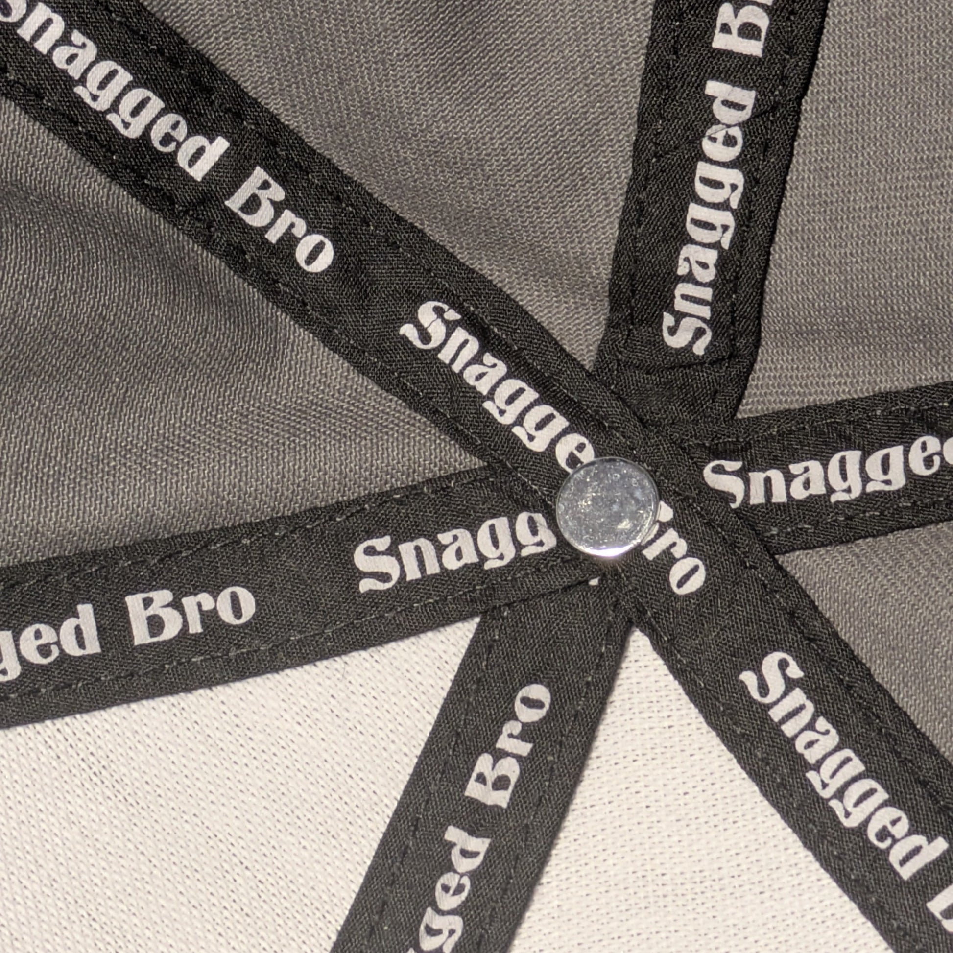 Close-up of a cap with 'Snagged Bro' branding on a gray and beige background