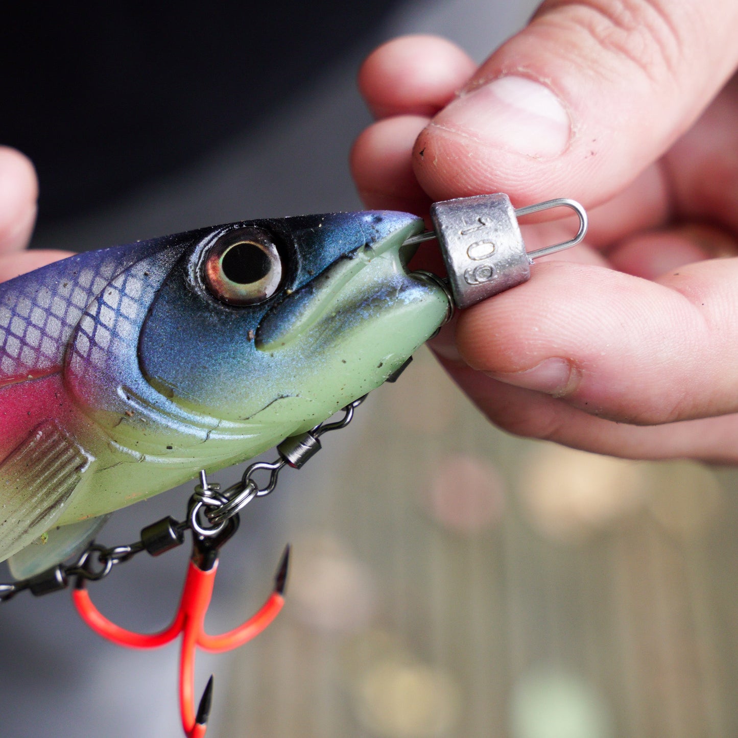 Close-up of a fishing lure with 10g cheb weight and UV hooks being held by hands with a blurred background