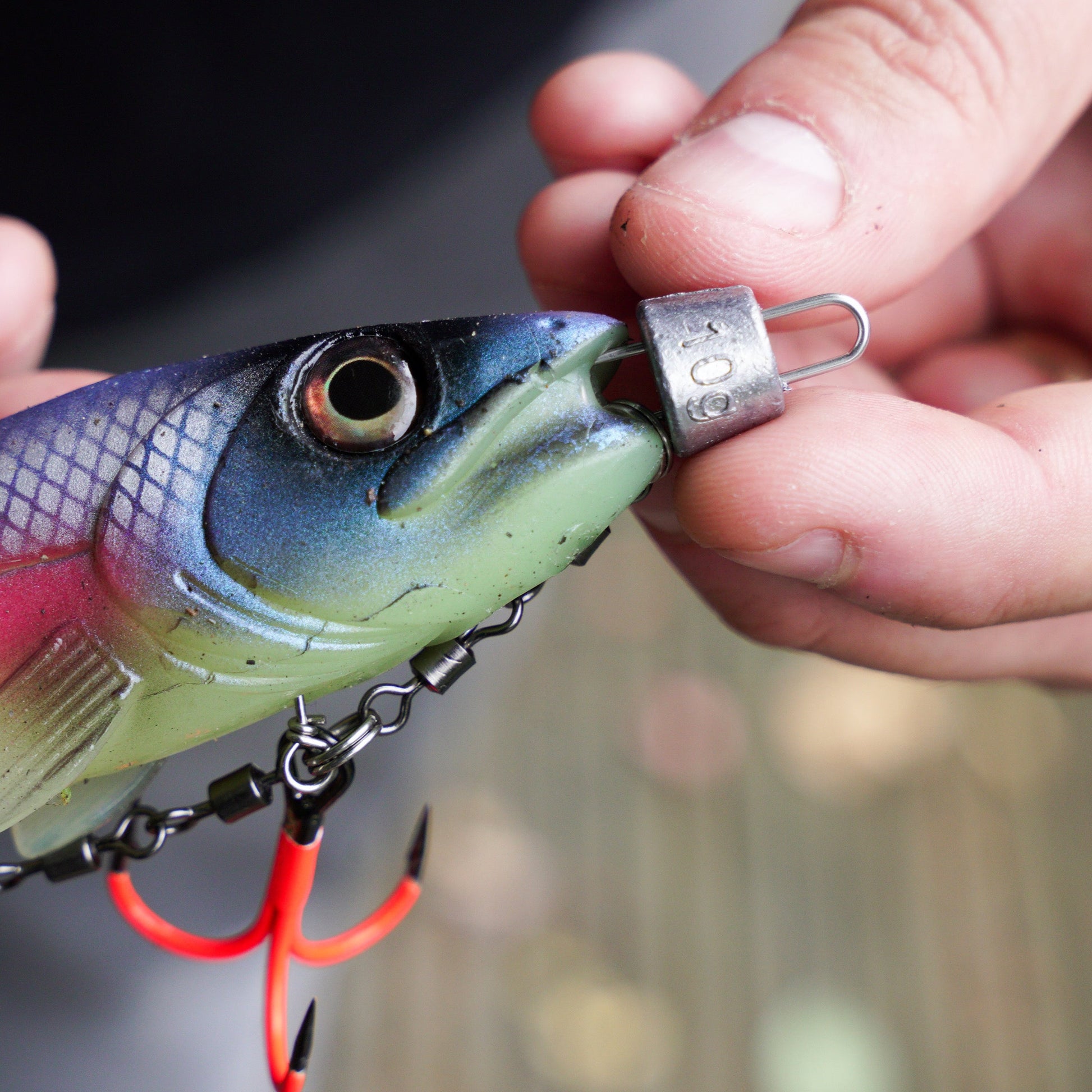 Close-up of a fishing lure with 10g cheb weight and UV hooks being held by hands with a blurred background